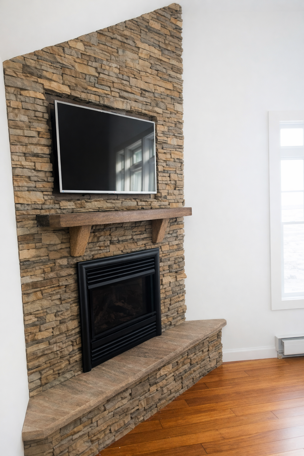 Living room fireplace with a stone surround, wooden mantle, and a mounted flat-screen TV above it, with a window to the right.