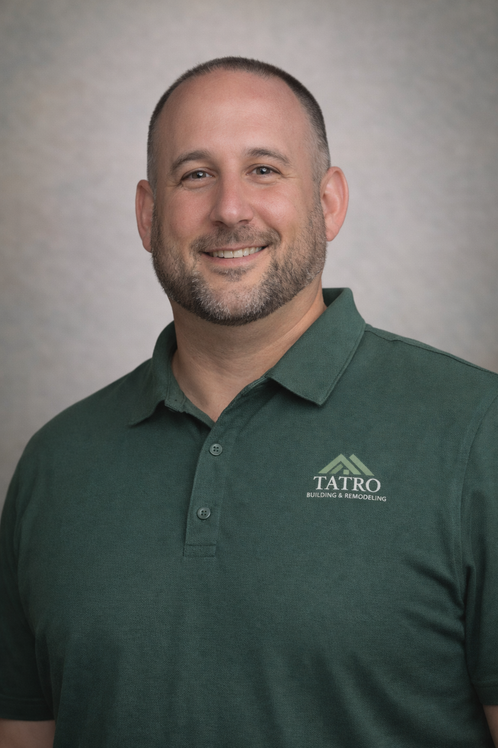 Headshot of a man with a beard smiling, wearing a green polo shirt with a logo that says TATRO Building & Remodeling.