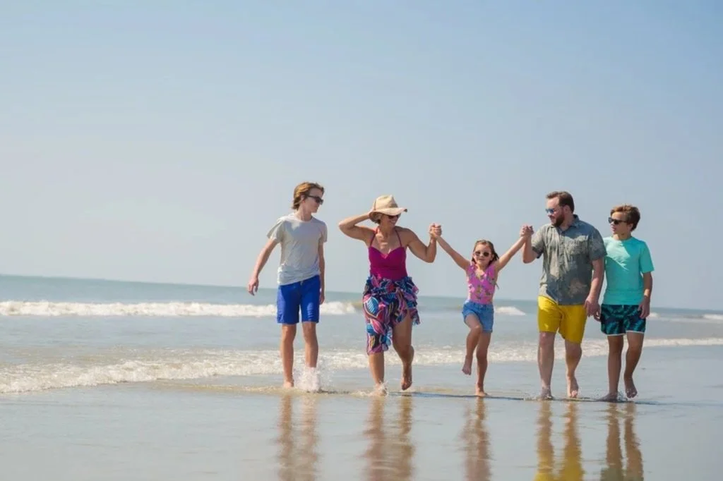 Family holding hands and walking along the beach near the ocean during daytime