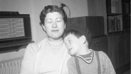 A woman and a boy sit close together, the boy resting his head on the woman's shoulder in a black-and-white photo.