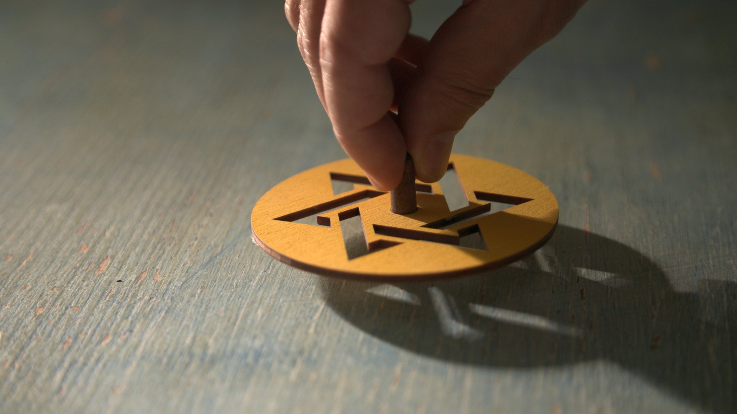 A hand rotates a wooden spinning top with a star-shaped cutout on a textured surface.