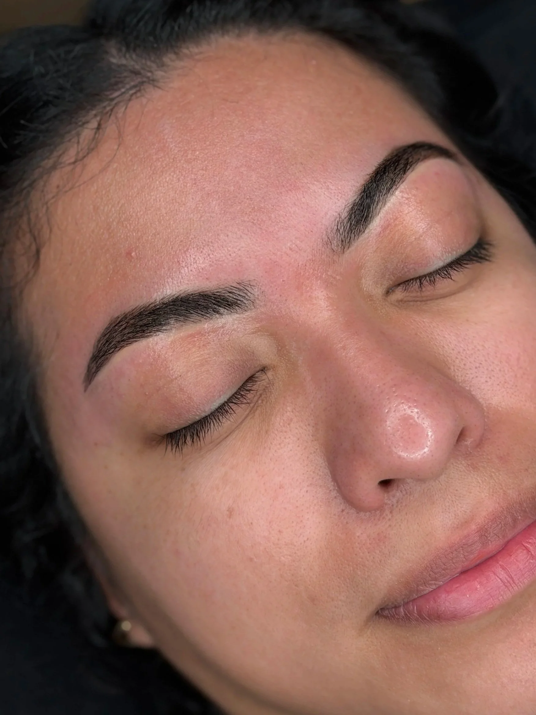 Close-up of a woman's face with her eyes closed, showcasing well-groomed eyebrows and clear skin.