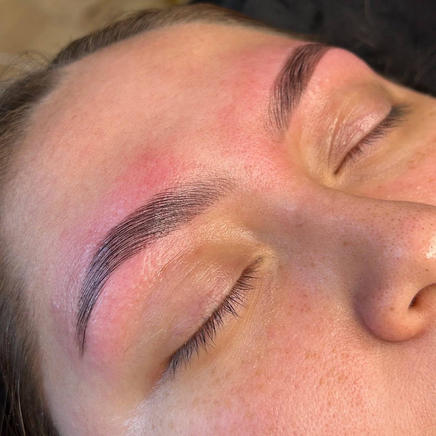 Close-up of a person's face showing freshly done eyebrow microblading, with smooth, well-defined brows and clear skin.