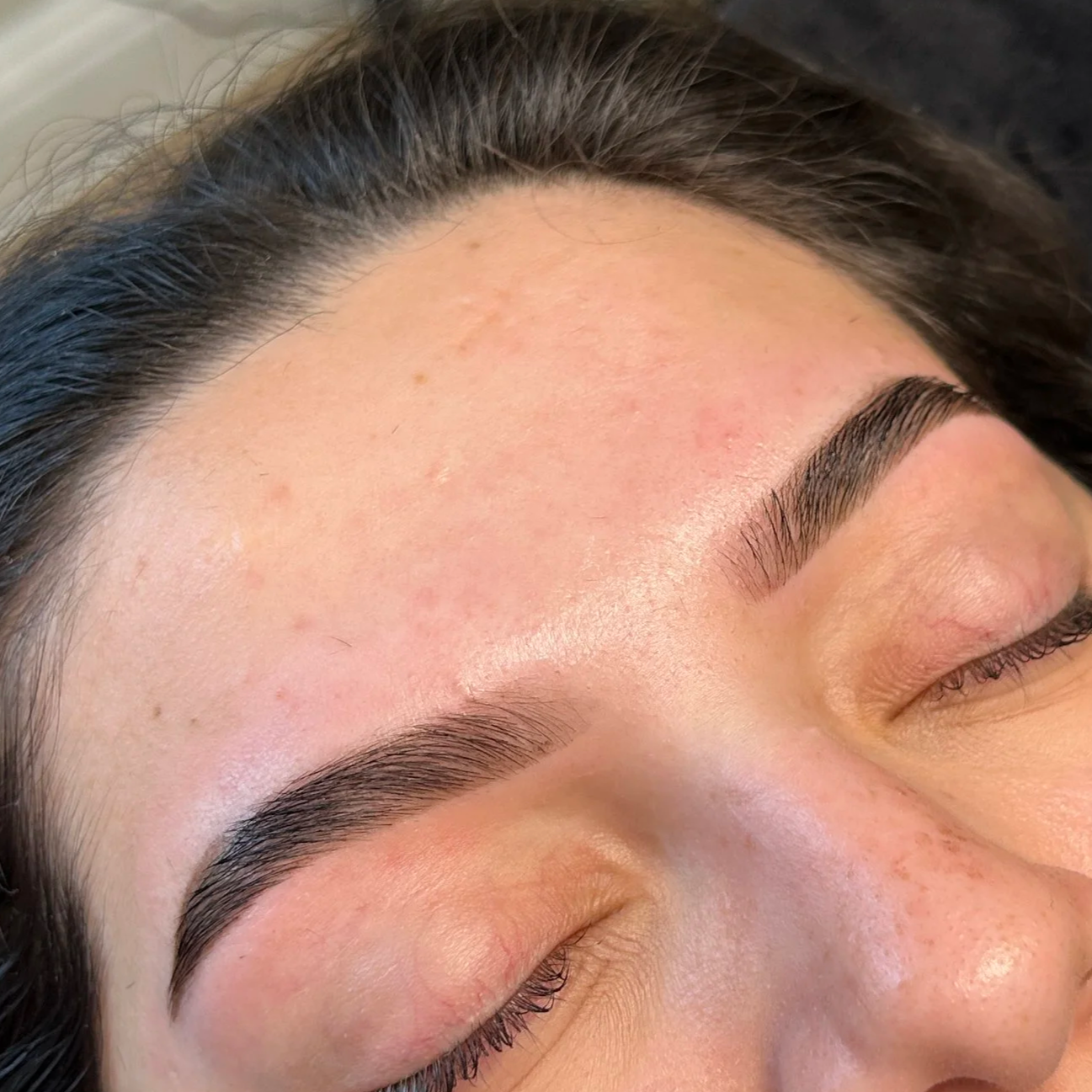 Close-up of a woman's face with freshly done eyebrow waxing or threading, showing well-shaped, dark, and arched eyebrows with smooth skin.