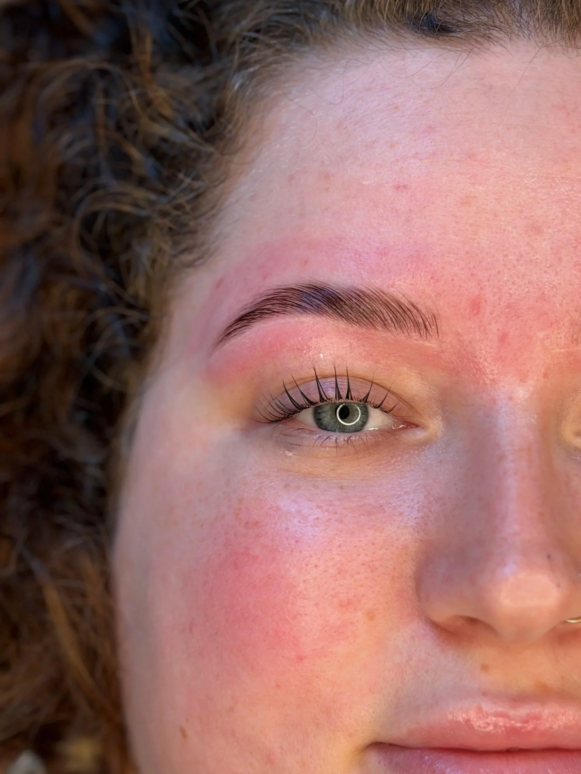 Close-up of a woman's face focusing on her eye, eyebrow, and part of her forehead, with curly hair visible on the left side.