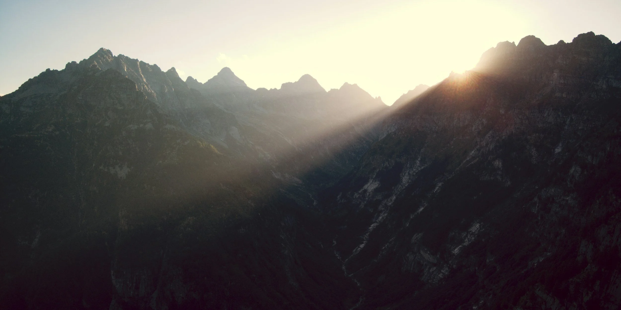 Sun rising over a mountain range with rugged peaks and deep valleys.