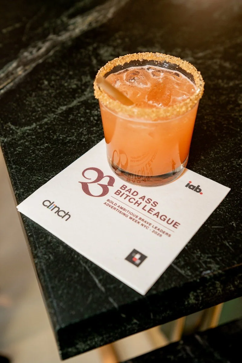 A pink cocktail with ice and a lemon wedge, rimmed with sugar, placed on a white paper napkin on a black marble surface.