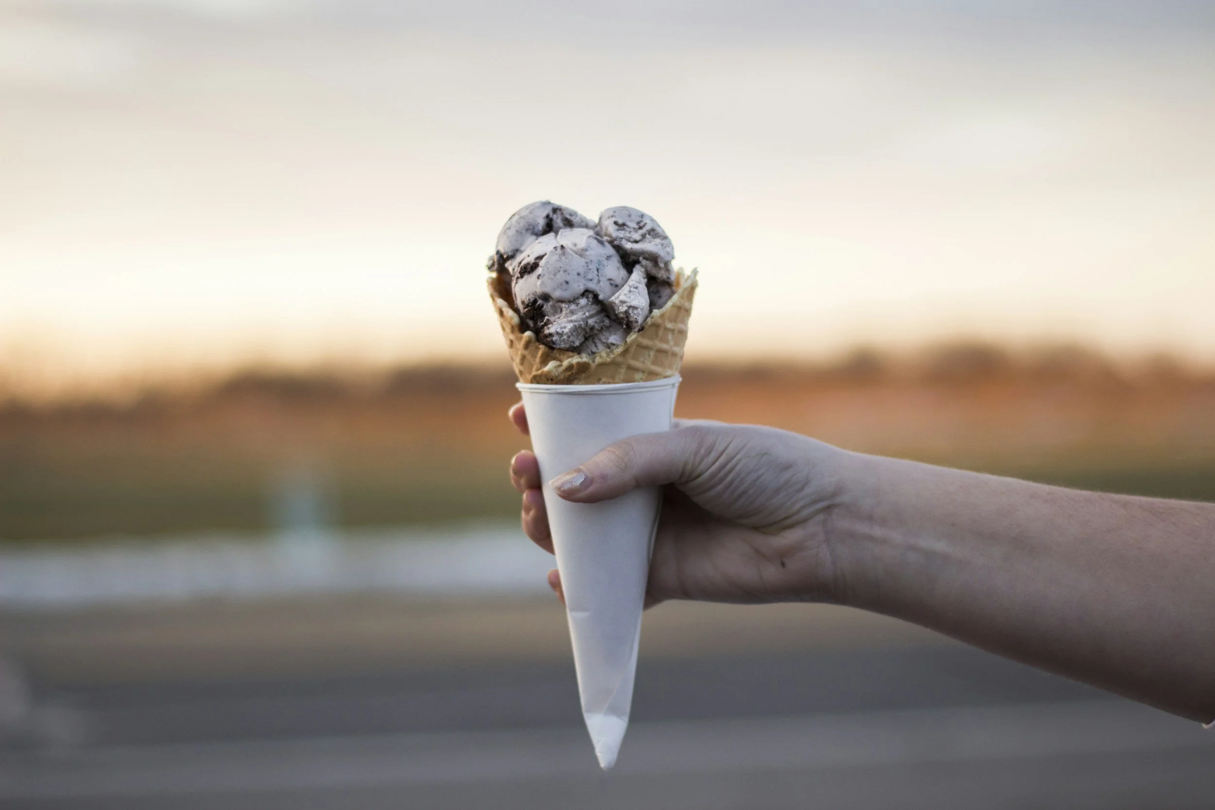 Hand holding an ice cream cone with chocolate chip ice cream against a sunset background.