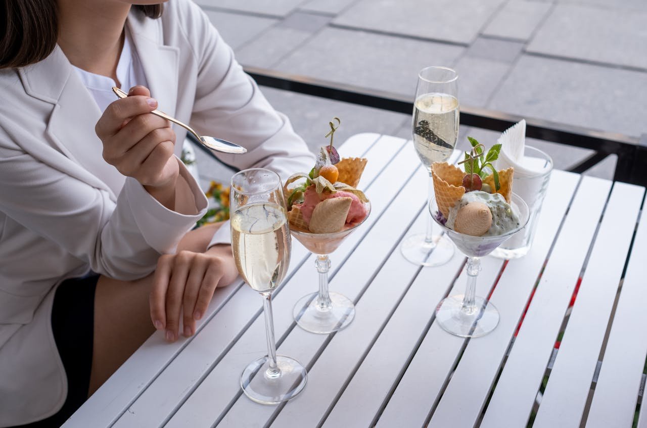 Woman holding a spoon with two glasses of champagne and two ice cream sundaes on a white table.