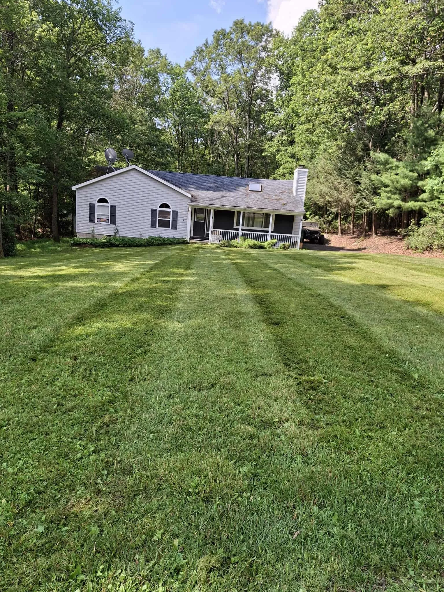 A white house with a screened porch surrounded by a green lawn and trees.