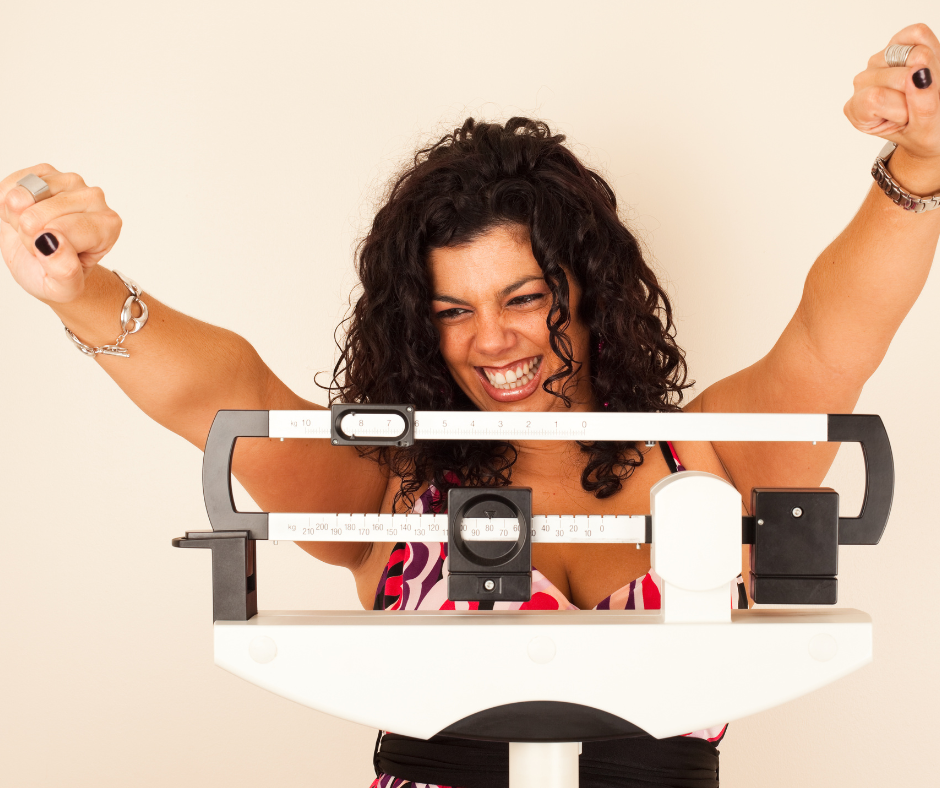 Woman smiling and flexing her arms while standing on a scale.