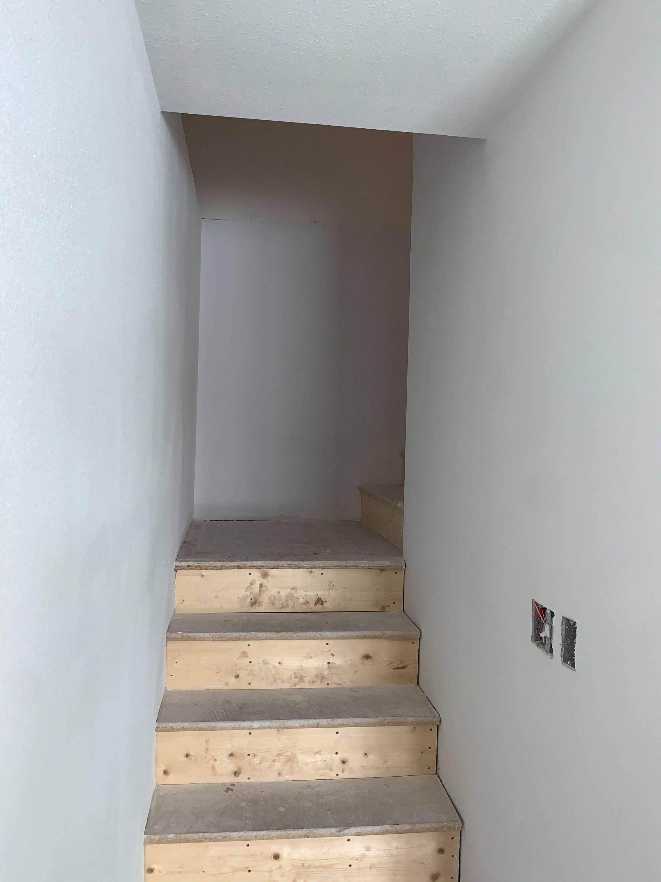 Unfinished staircase with wooden steps and gray concrete treads, inside a residential space under construction.