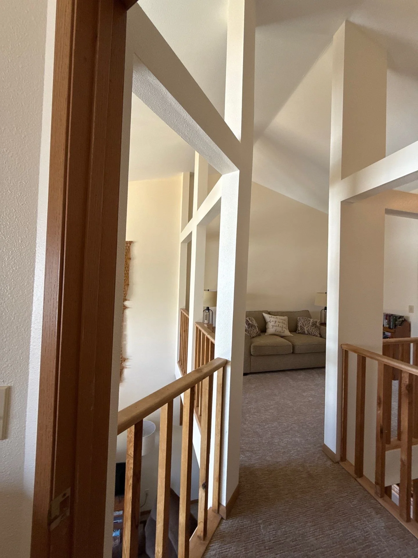 View of a upstairs hallway with wooden railings, leading to a living room with a beige sofa and decorative pillows.