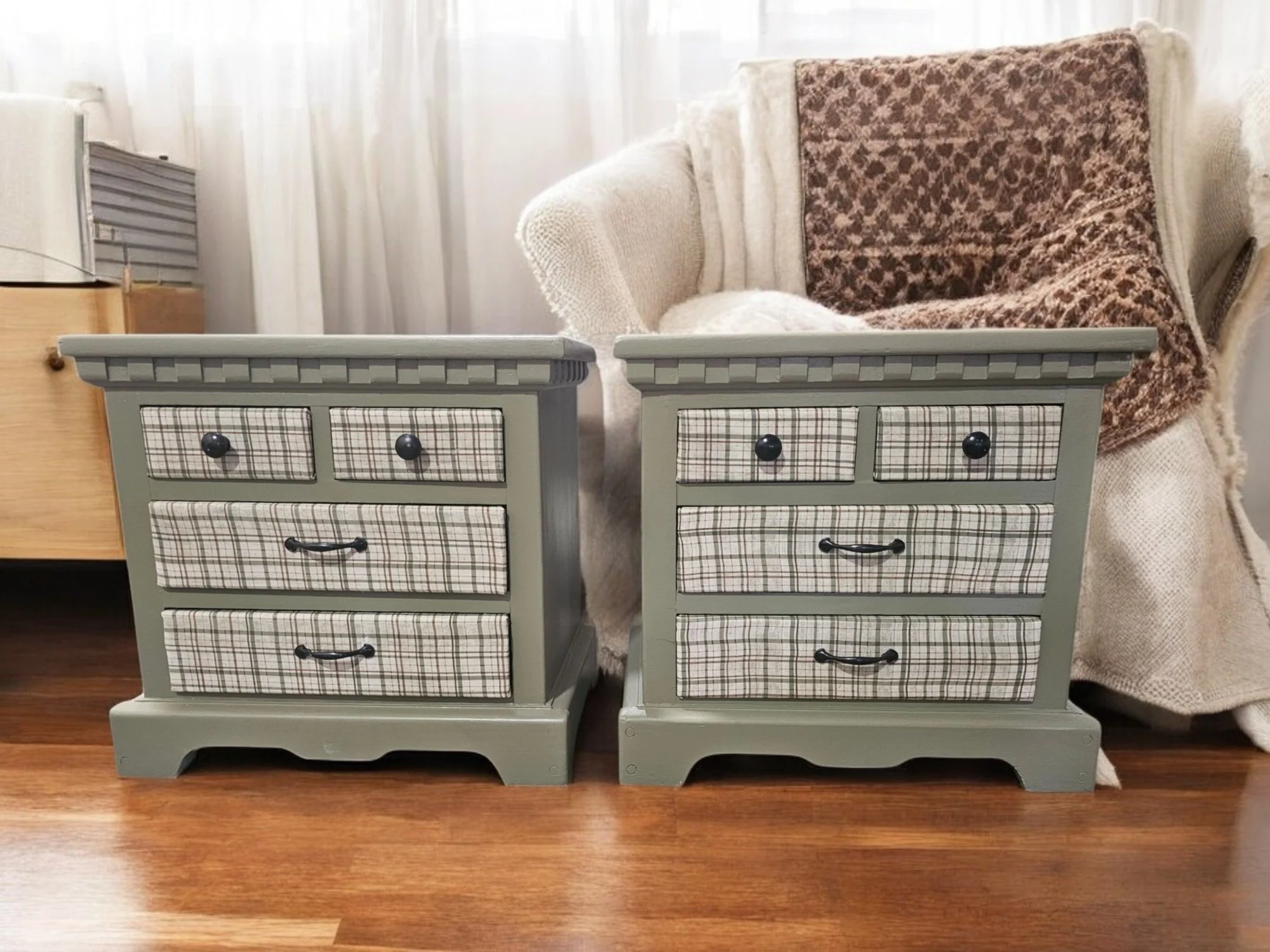 Two small vintage-style nightstands with plaid drawers and black knobs, placed side by side on a wooden floor, in front of a cream-colored sofa with a brown patterned blanket draped over it.