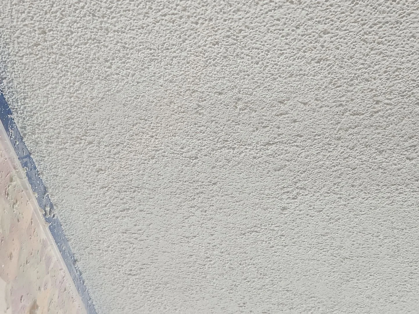 Close-up of a textured ceiling with a section of painted wall in the bottom left corner.
