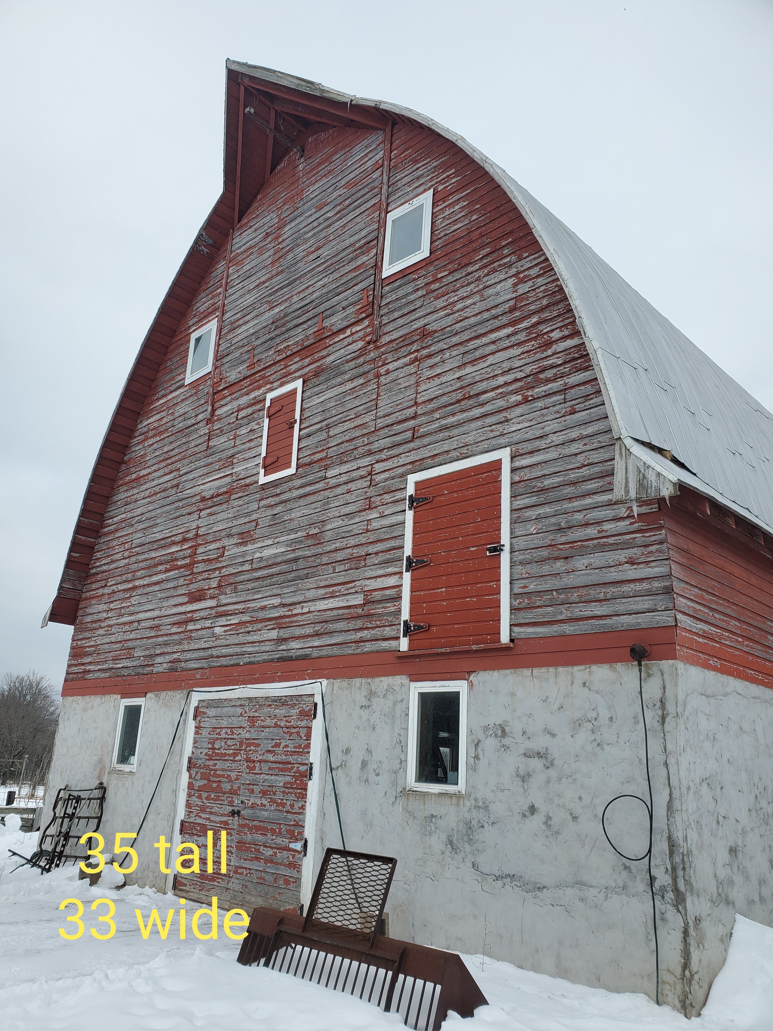 A tall red barn with peeling paint and multiple small windows, situated on a snow-covered ground.