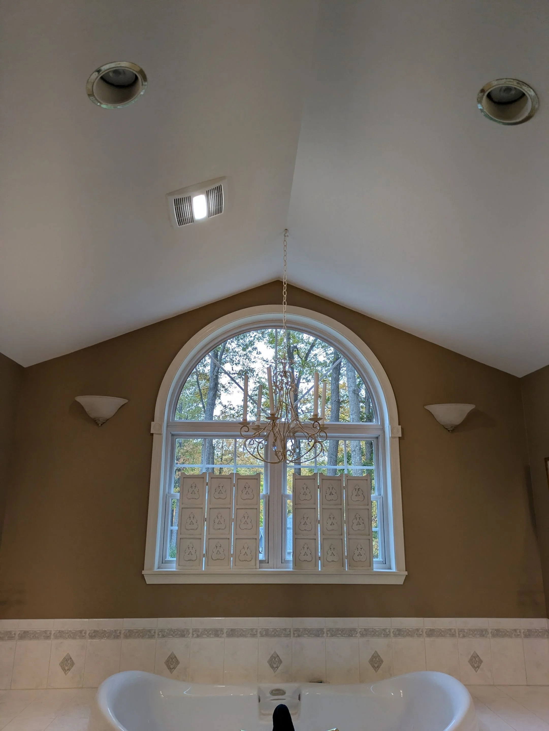 Bathroom with a large arched window, chandelier, and a bathtub.