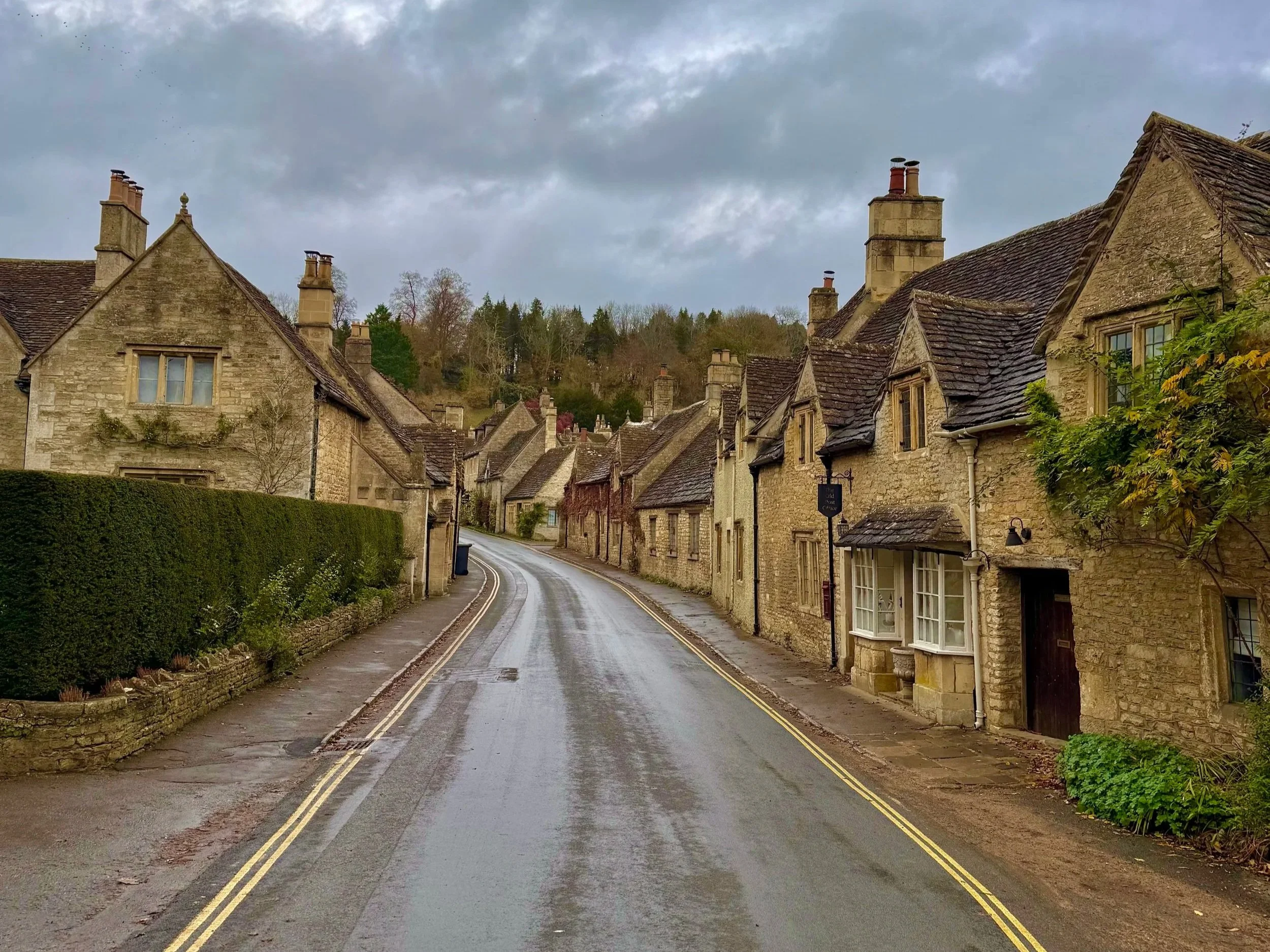 A narrow street lined with honey colored stone houses in Castle Combe UK.