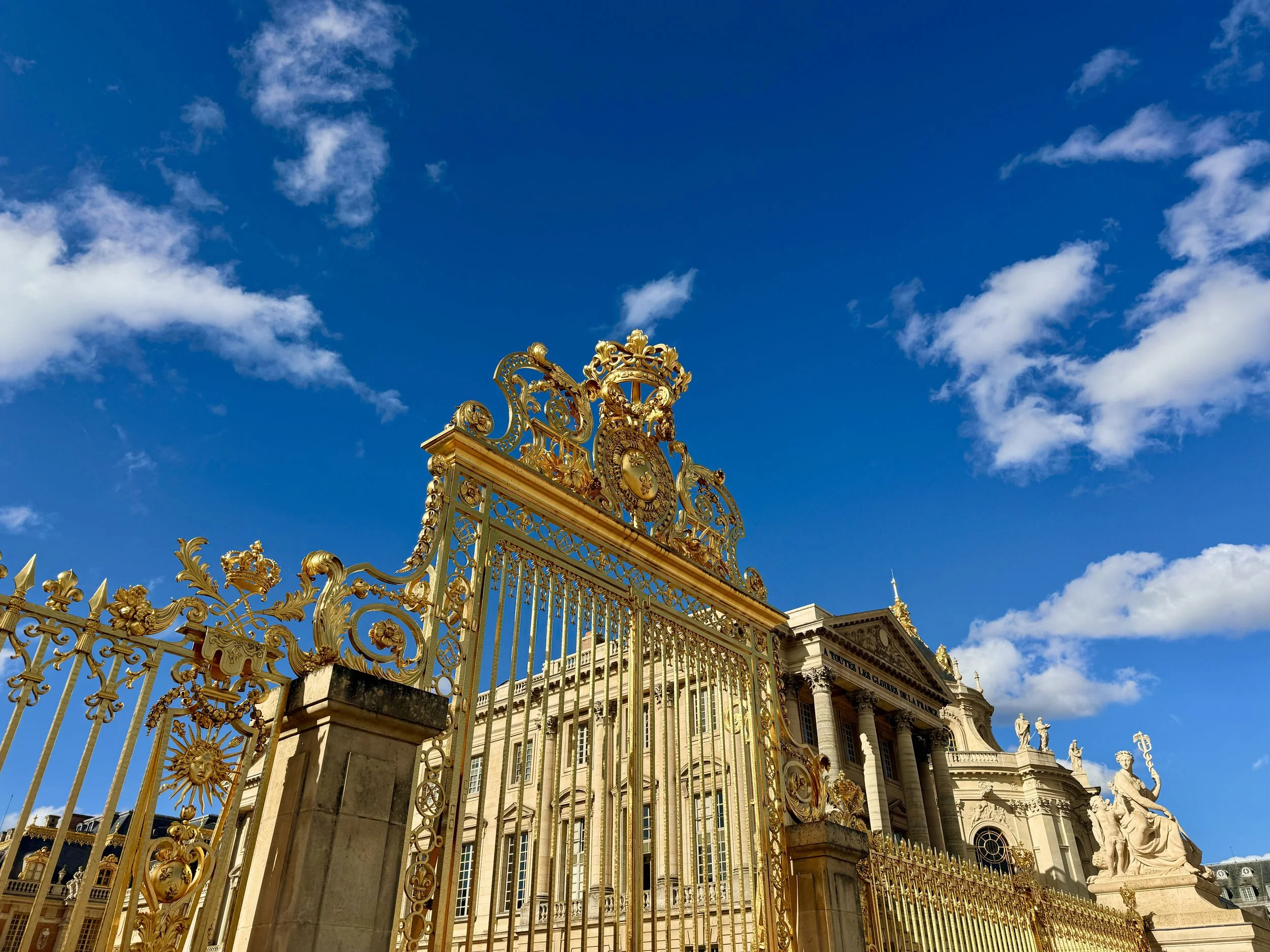 Gilded ornate gate leading to the entrance of Versailles Palace.