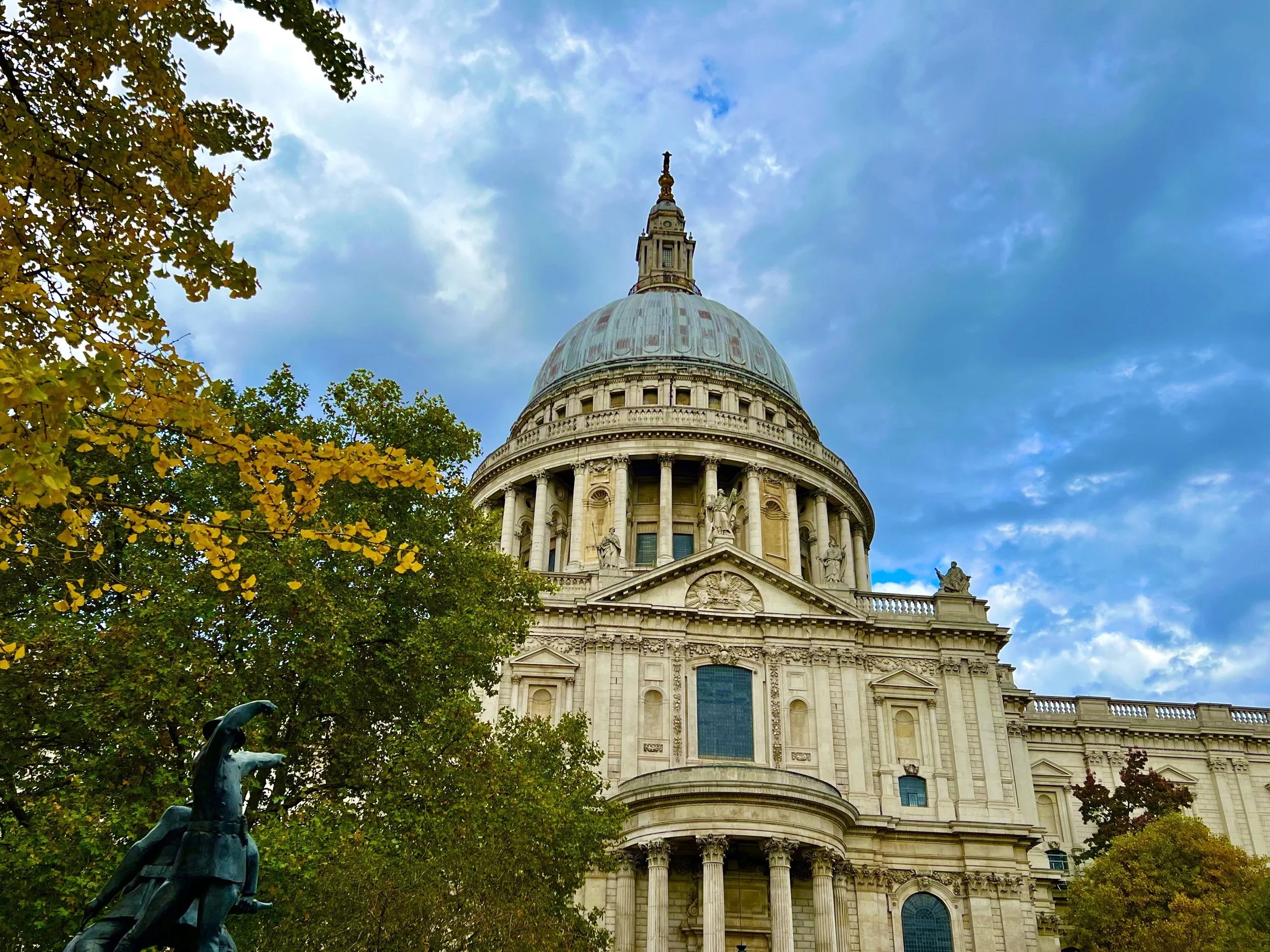 The image features St. Paul’s Cathedral with its prominent dome in London, framed by trees with autumn foliage.