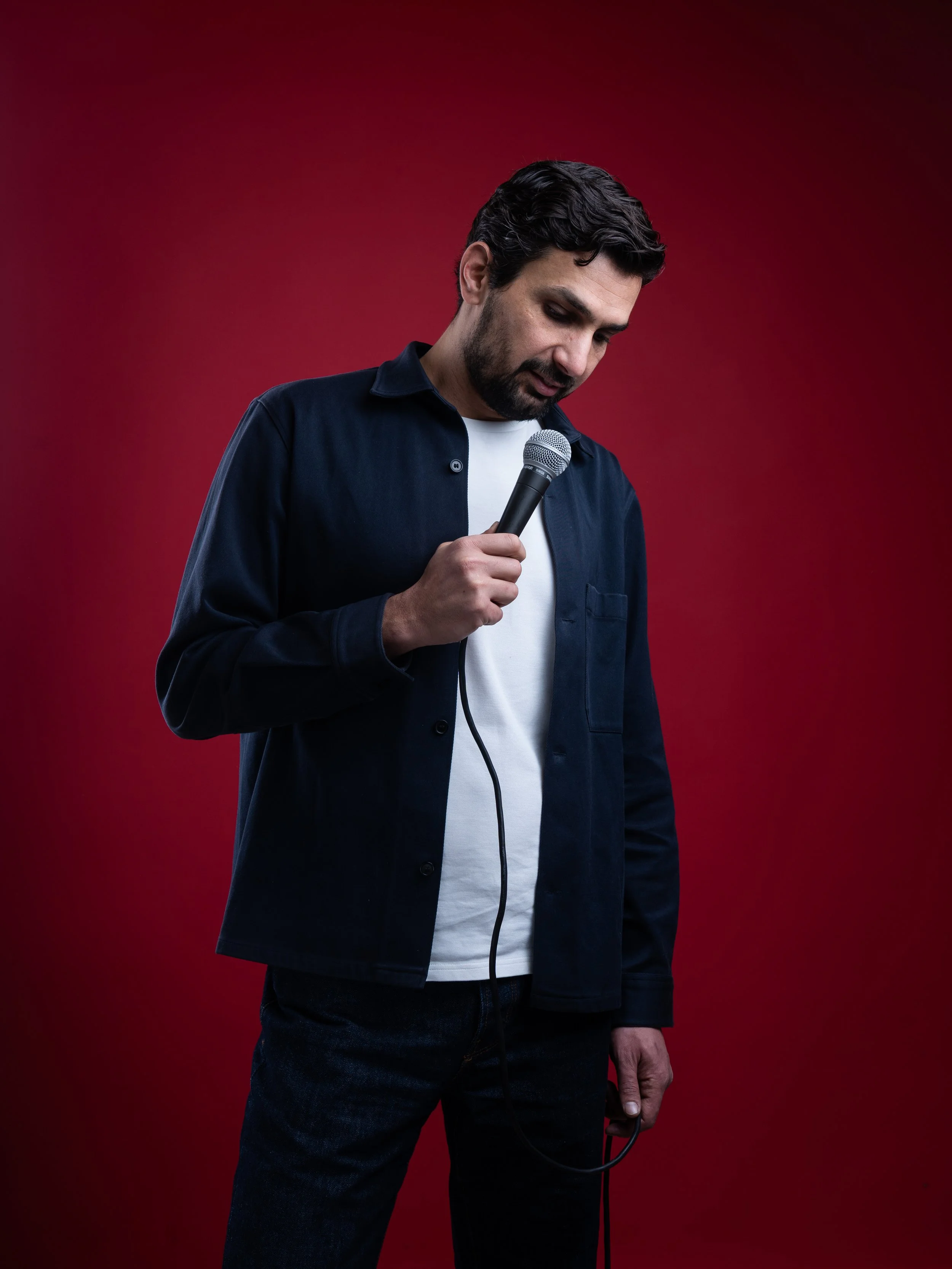 Alaa Abu Diab holding a microphone, looking down, against a red background.