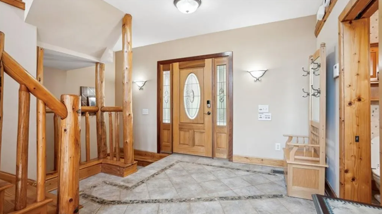 Entryway with wooden front door, tiled floor, and wooden staircase railing in a home.