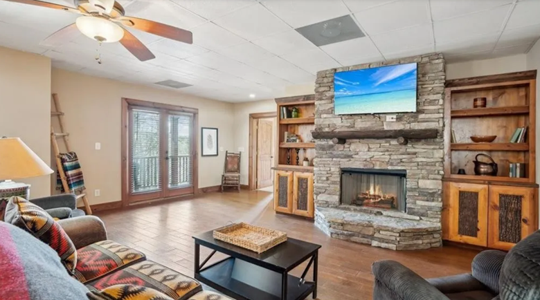 Living room with a stone fireplace, wooden cabinets, ceiling fan, hardwood floors, and a sliding glass door.