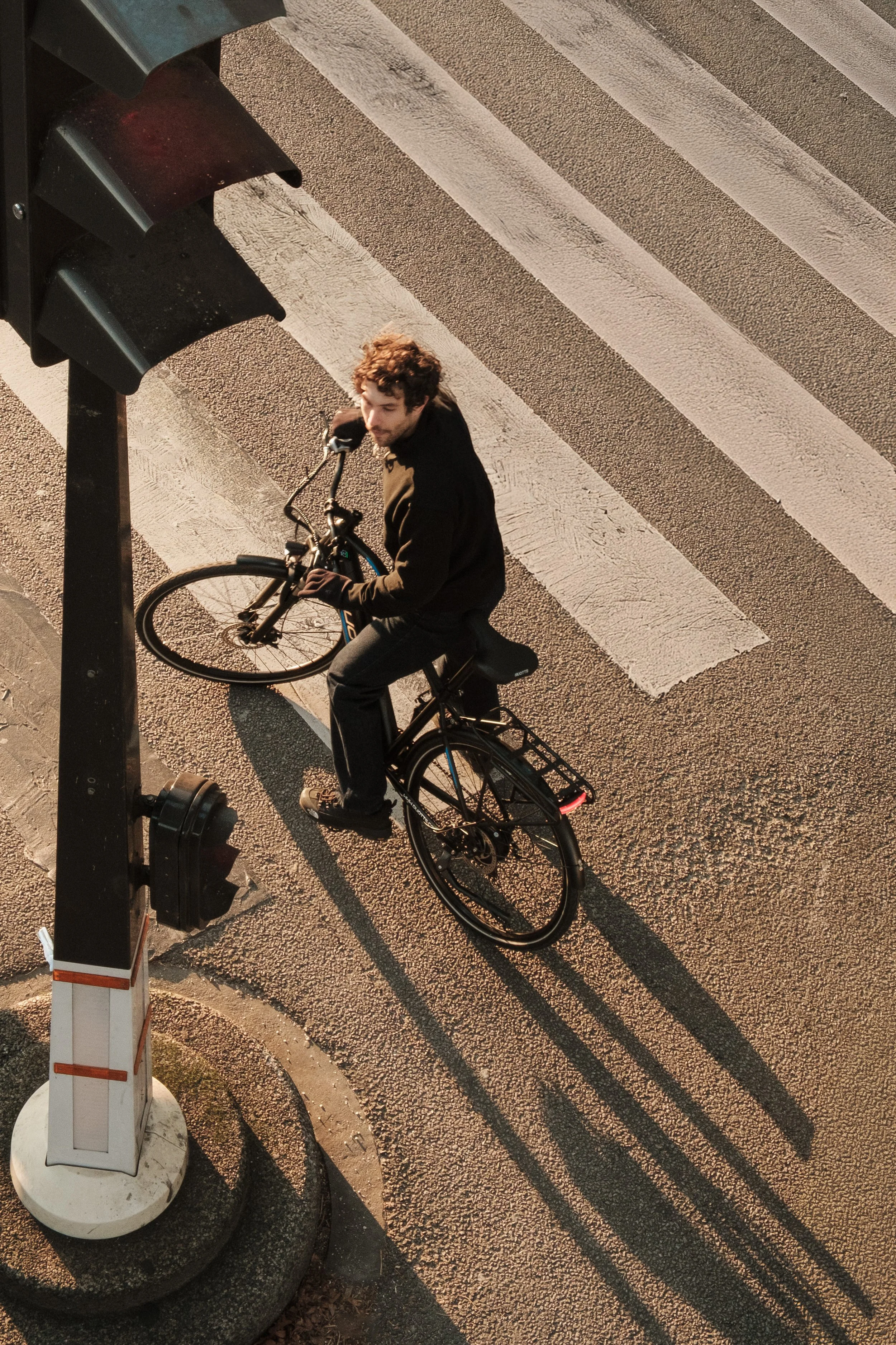 A man on a bicycle crossing a striped crosswalk seen from above, with a traffic light in the foreground.