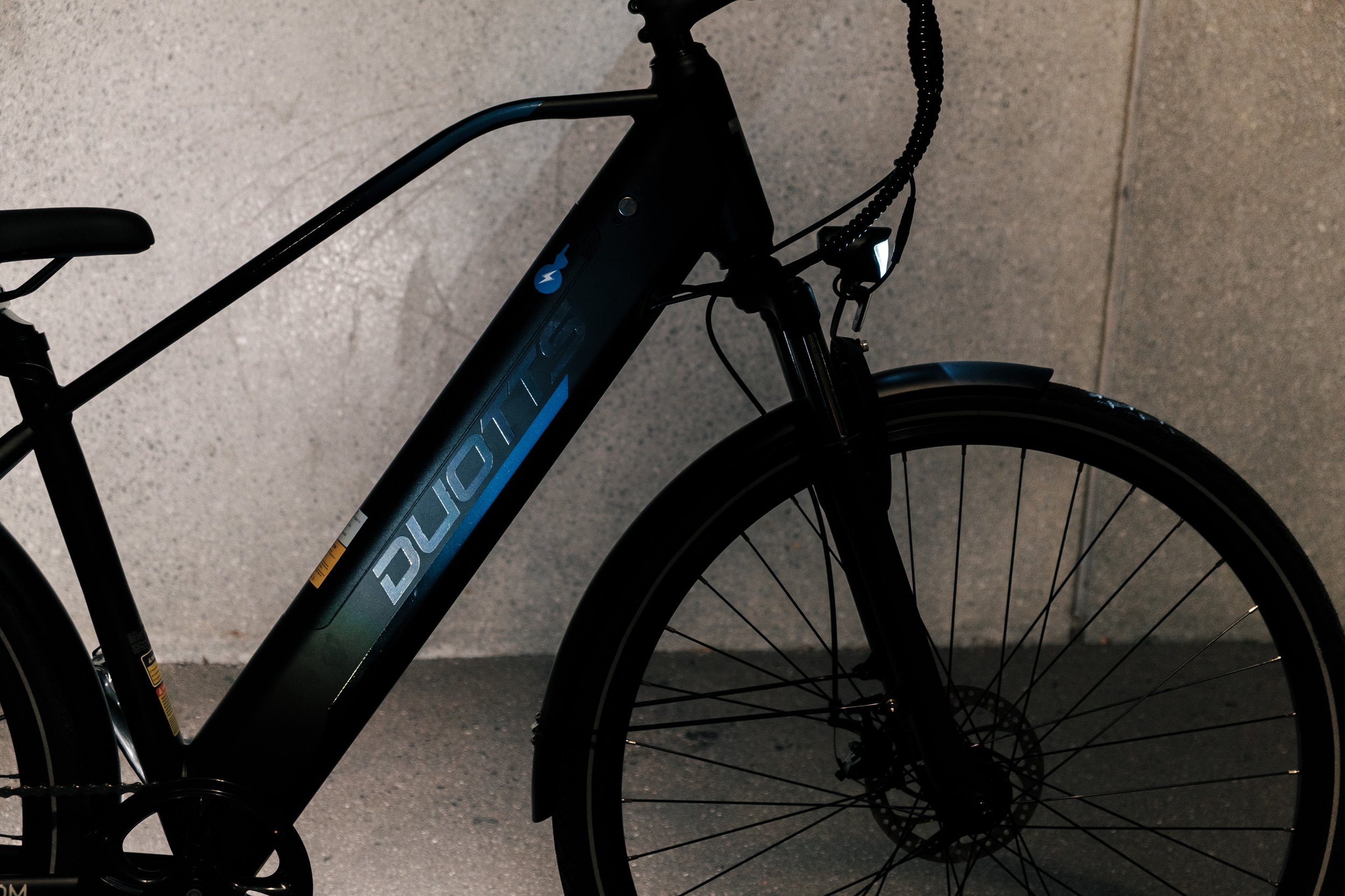Black Trek electric bicycle against a grey concrete wall, with the word 'DUALICT' on the frame.