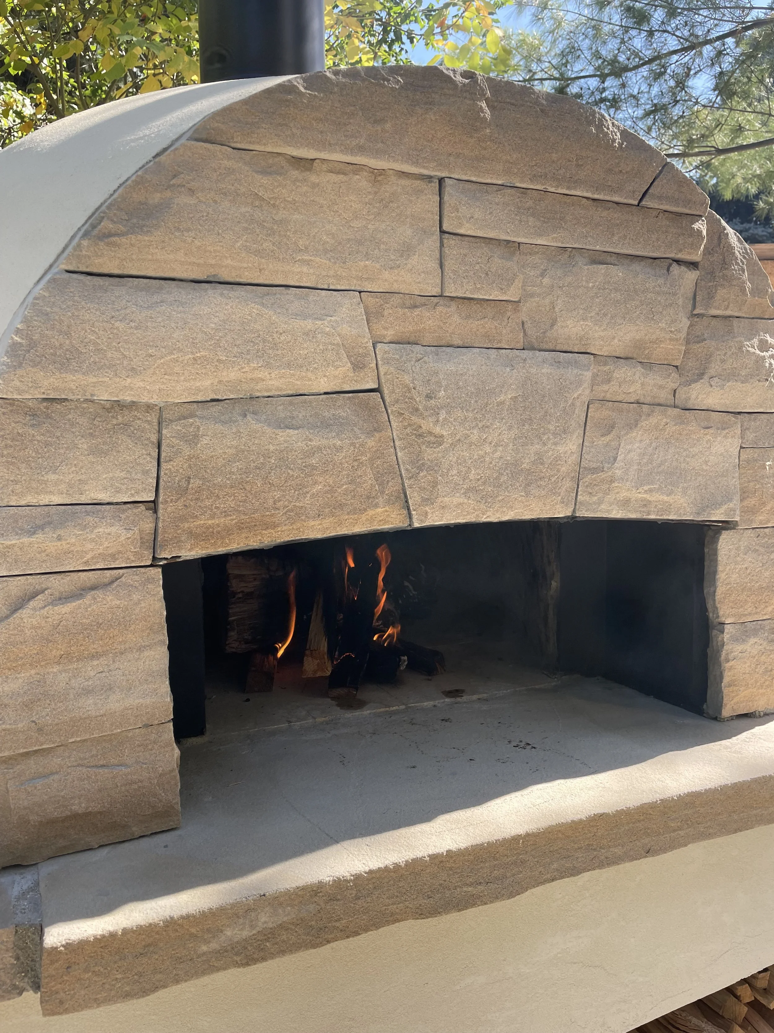 Outdoor stone pizza oven with glowing fire inside created and built by master stone masons Boulder StoneScapes.