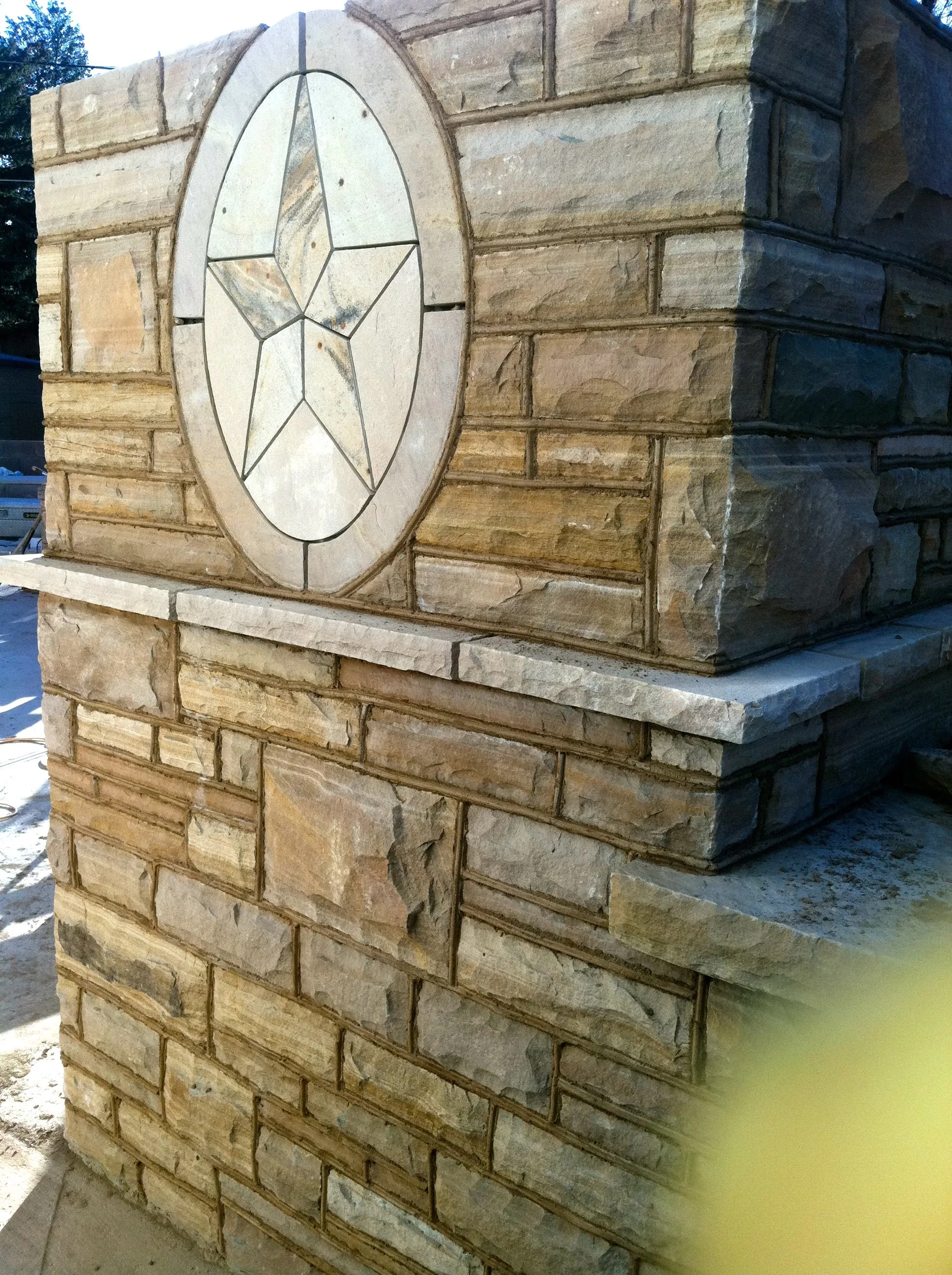 Close-up of a custom stone pillar with a decorative star emblem made of different stone pieces embedded in the upper part.