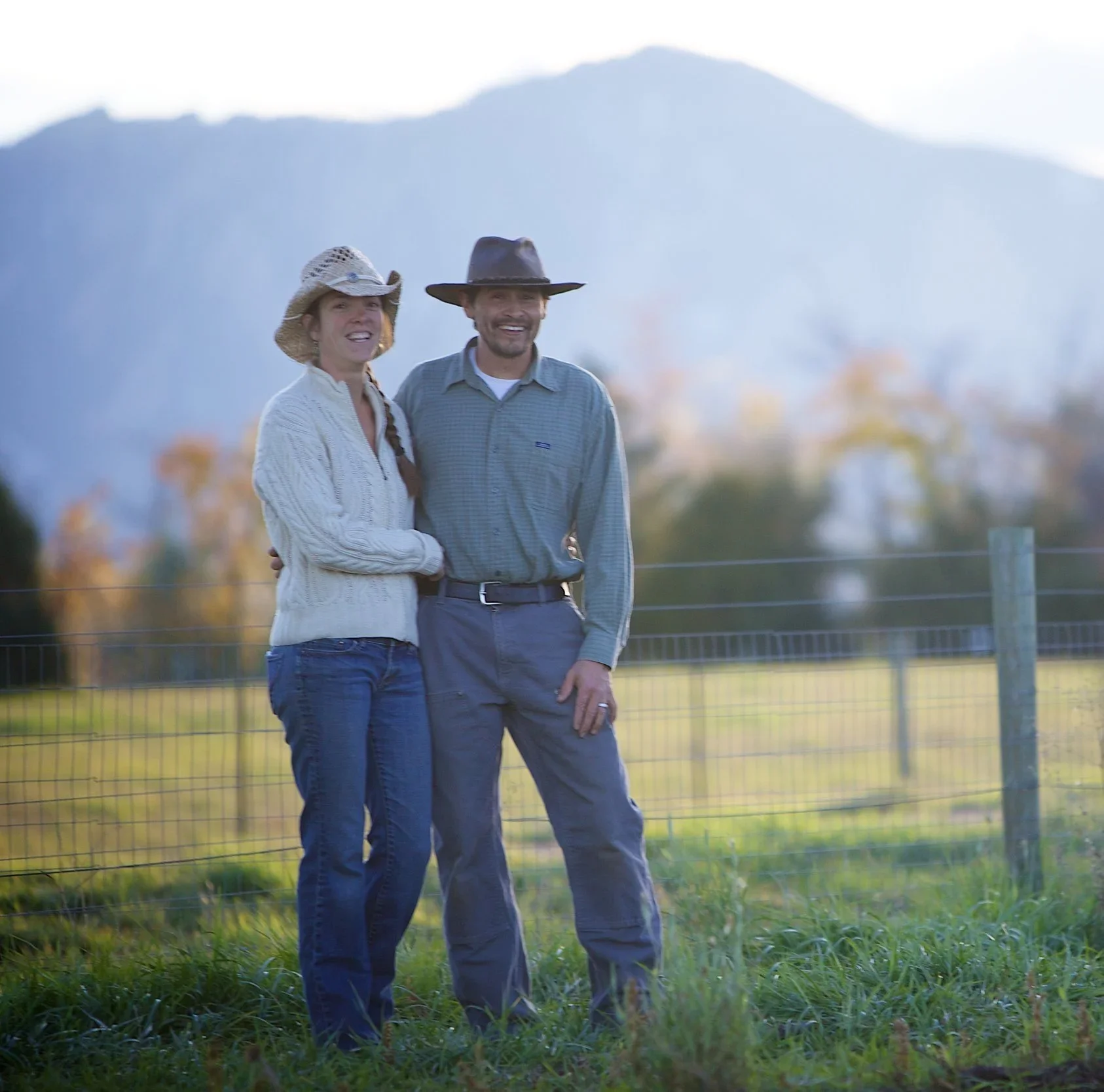 Expert stone masonry builders Brian & Amanda Scott of Boulder StoneScapes based out of Colorado smiling couple in cowboy hats standing together outdoors with mountains in the background.