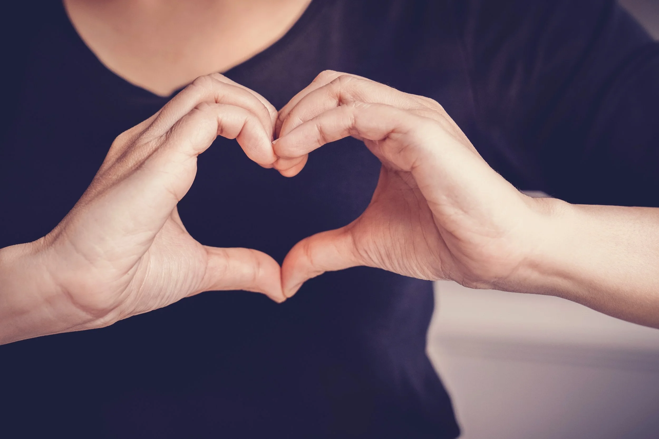 Two hands forming a heart shape against a dark background.