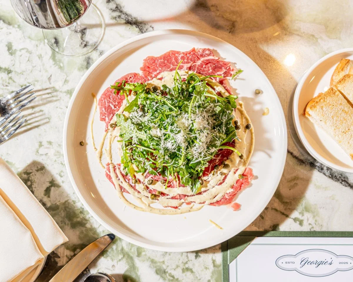 Georgie's beef carpaccio is topped with arugula salad and grated cheese, garnished with capers and drizzled with a creamy sauce.