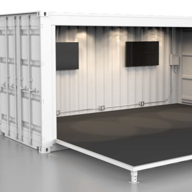 Inside a white shipping container with two wall-mounted monitors and a raised black platform floor.