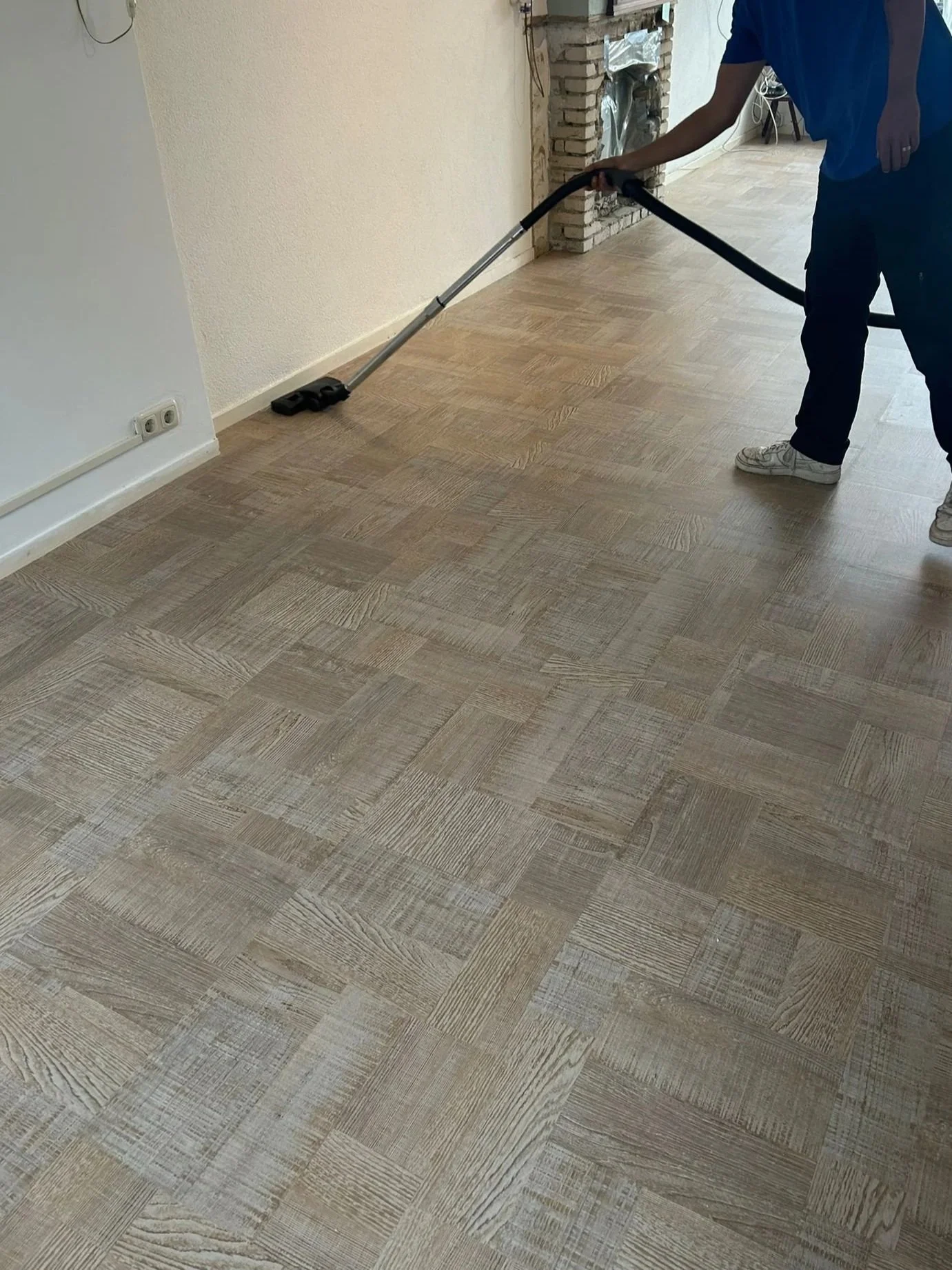 Person vacuuming a wooden floor in a room with a brick fireplace.