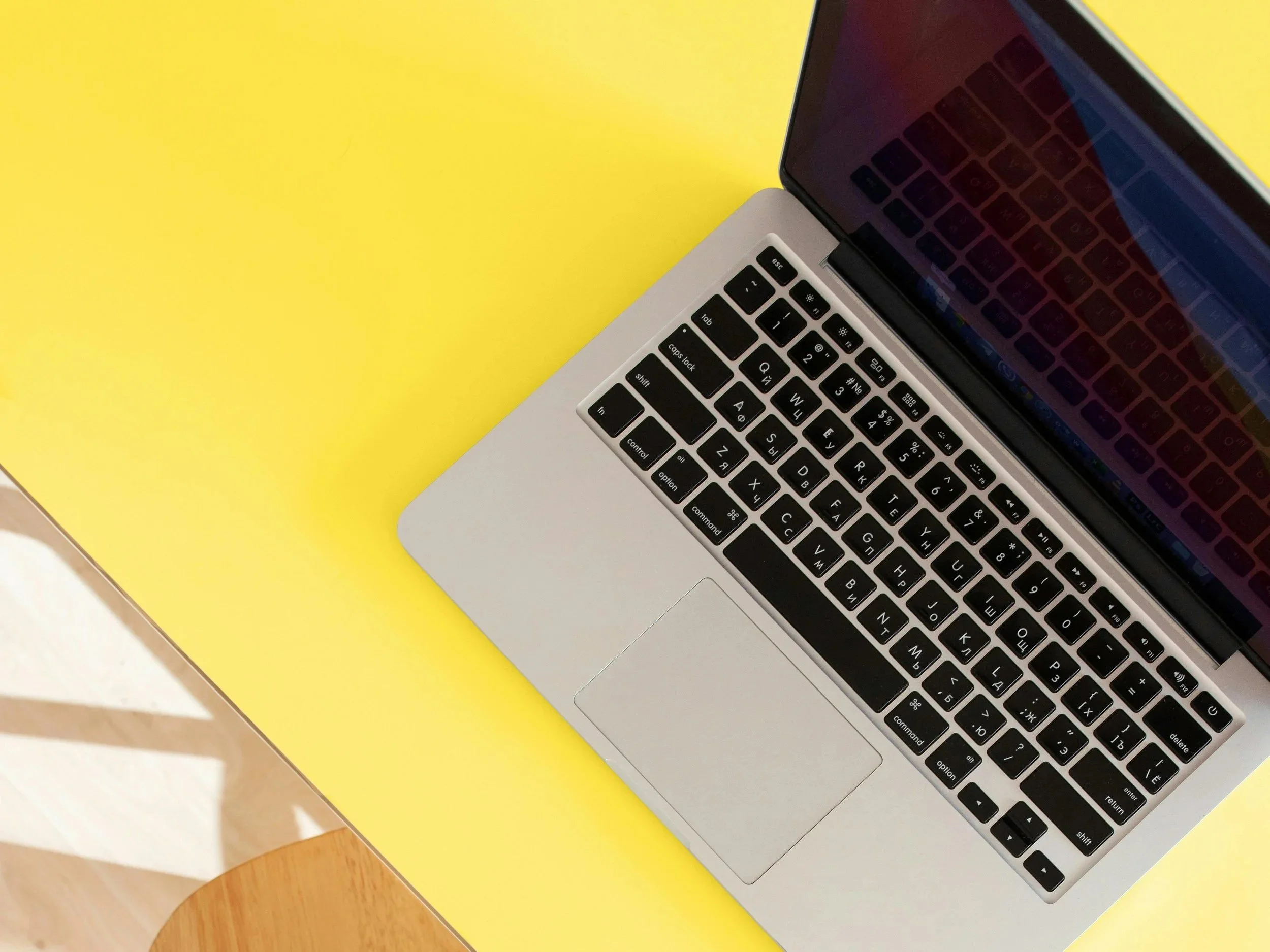 A silver laptop with a black keyboard sitting on a yellow surface.