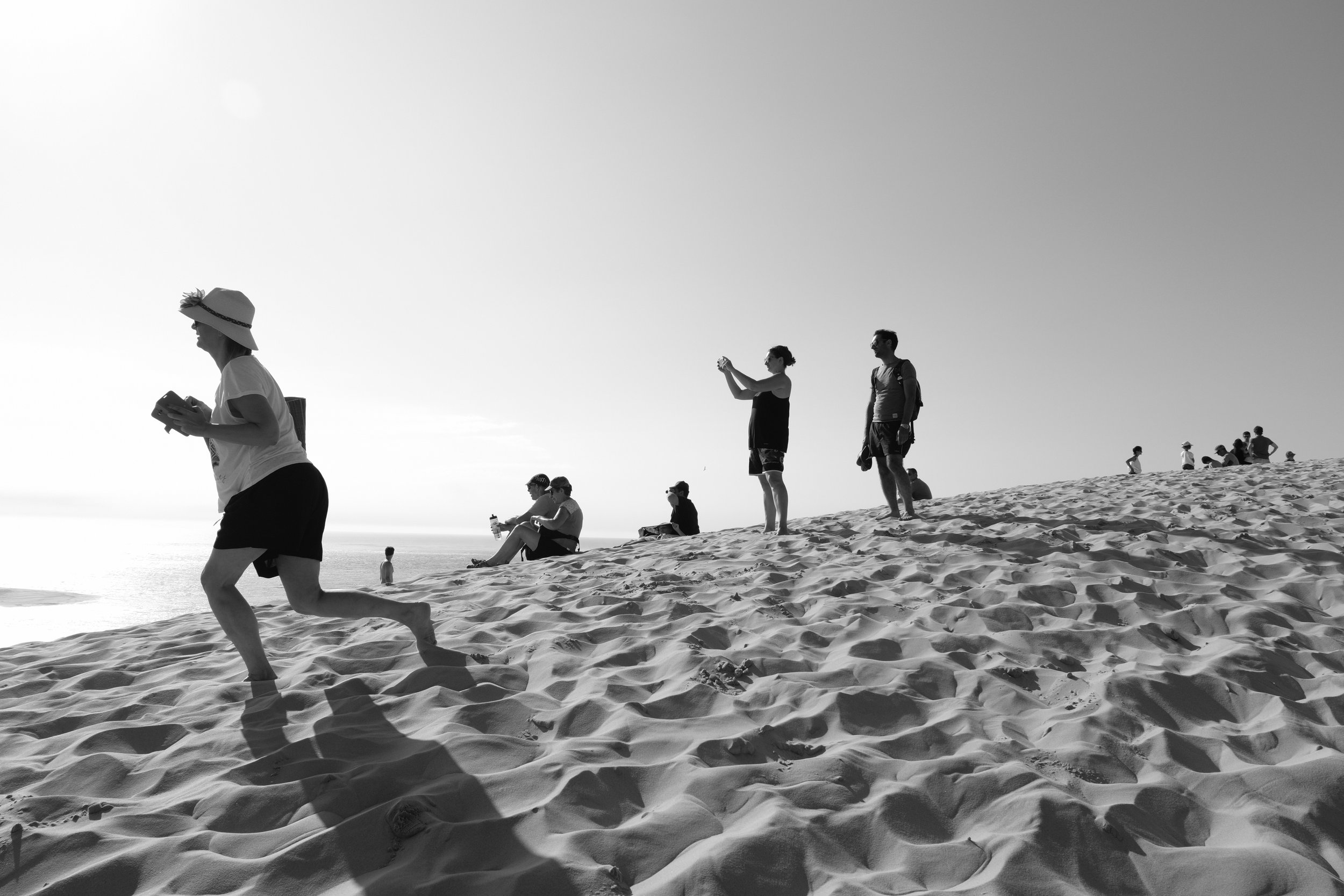People relaxing and taking photos on a sandy beach during sunset, with the ocean in the background.