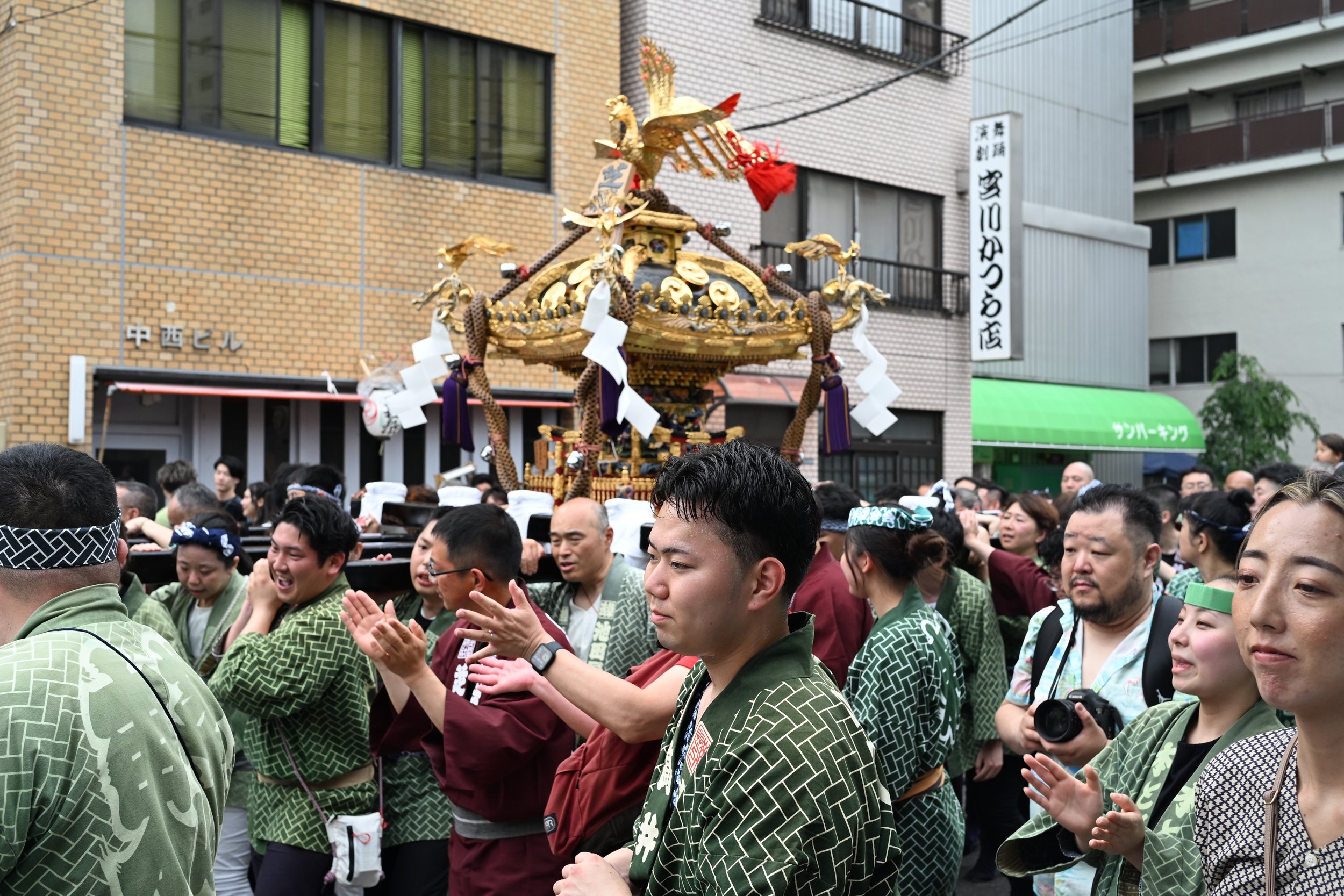 People participating in a traditional Japanese festival parade, carrying a decorated float with a golden ornament, dressed in colorful festival attire.