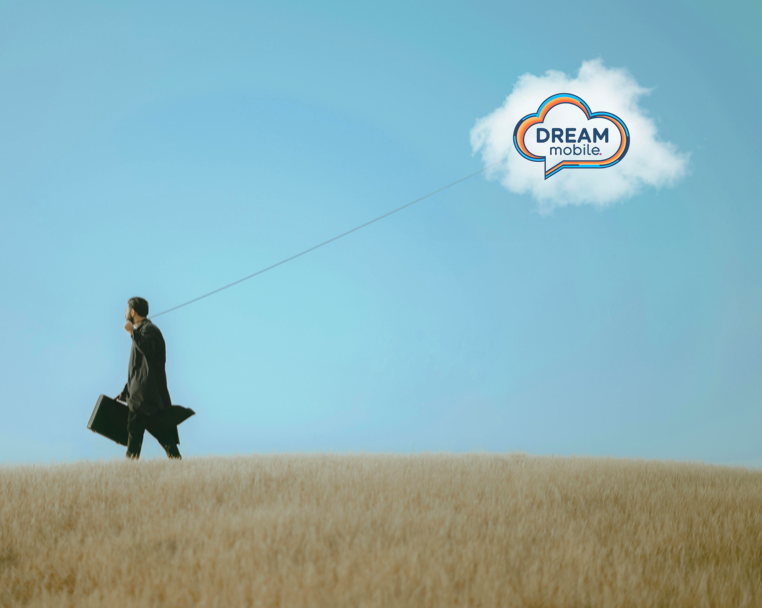 A businessman in a suit walking on a field, talking on a phone, carrying a briefcase, with a cloud-shaped logo reading 'DREAM mobile' floating in the sky attached to the ground by a string.