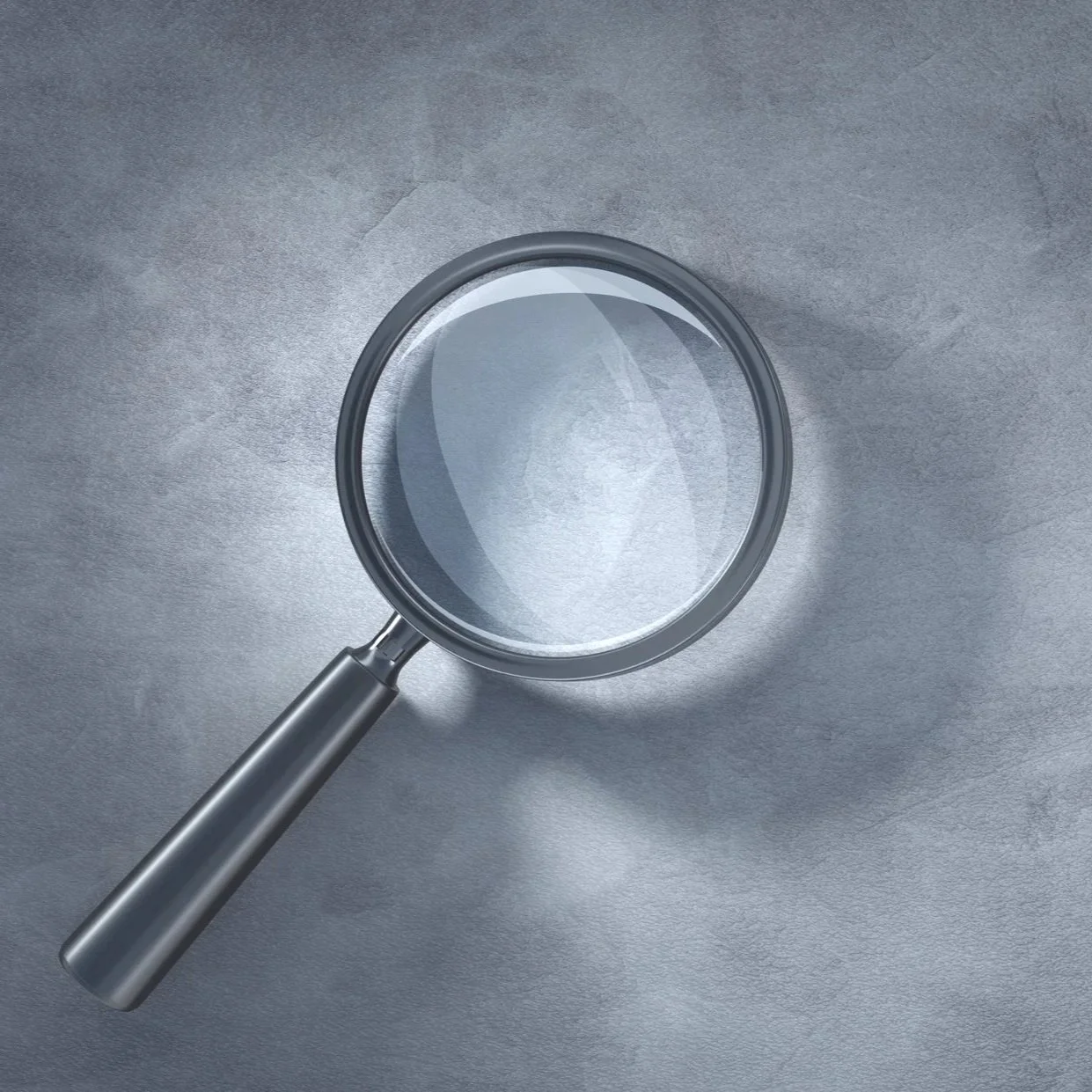 A stainless steel magnifying glass with a black handle placed on a gray textured surface.