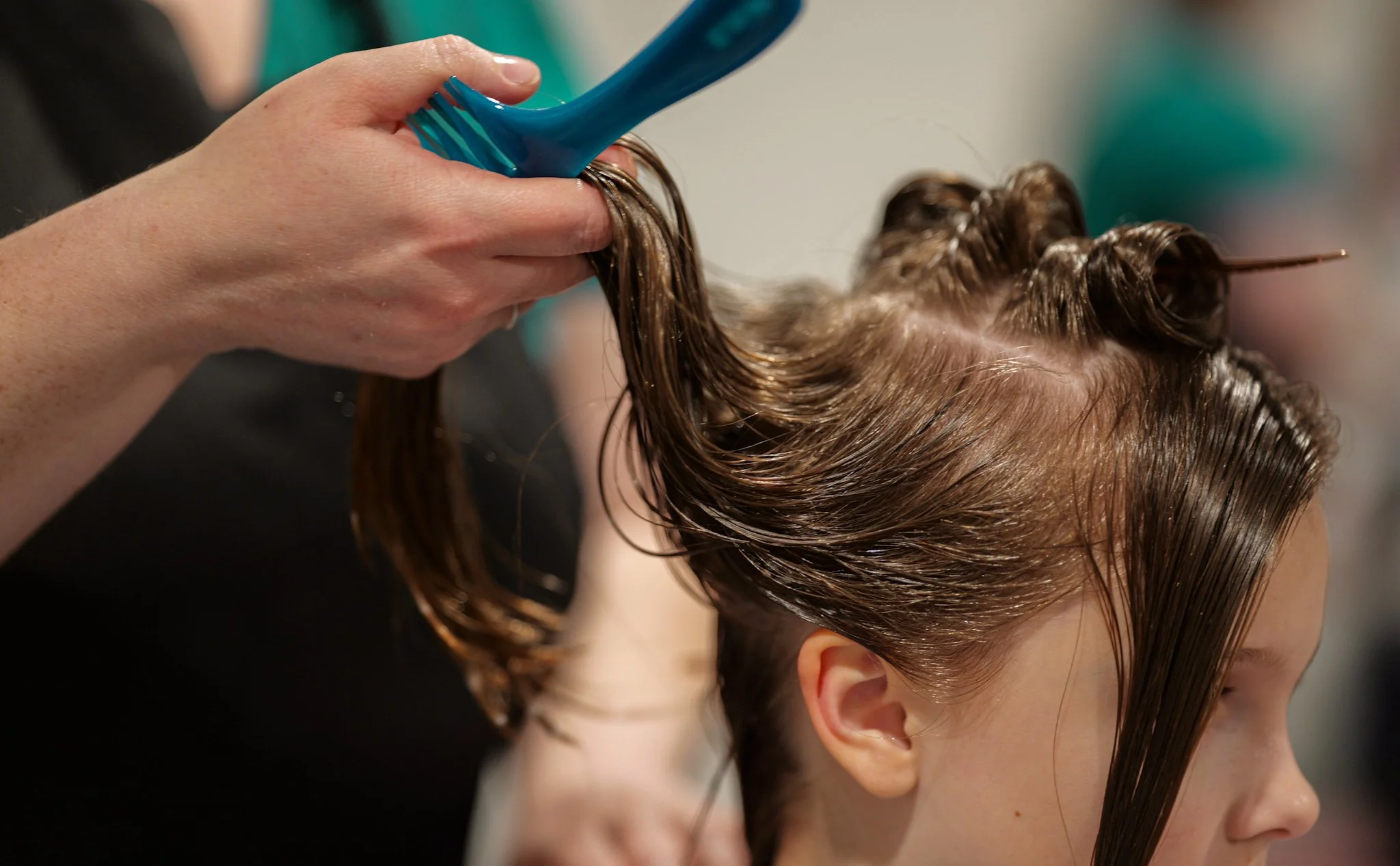 A hairstylist applying hair color or treatment to a young woman's wet, sectioned hair at a salon.