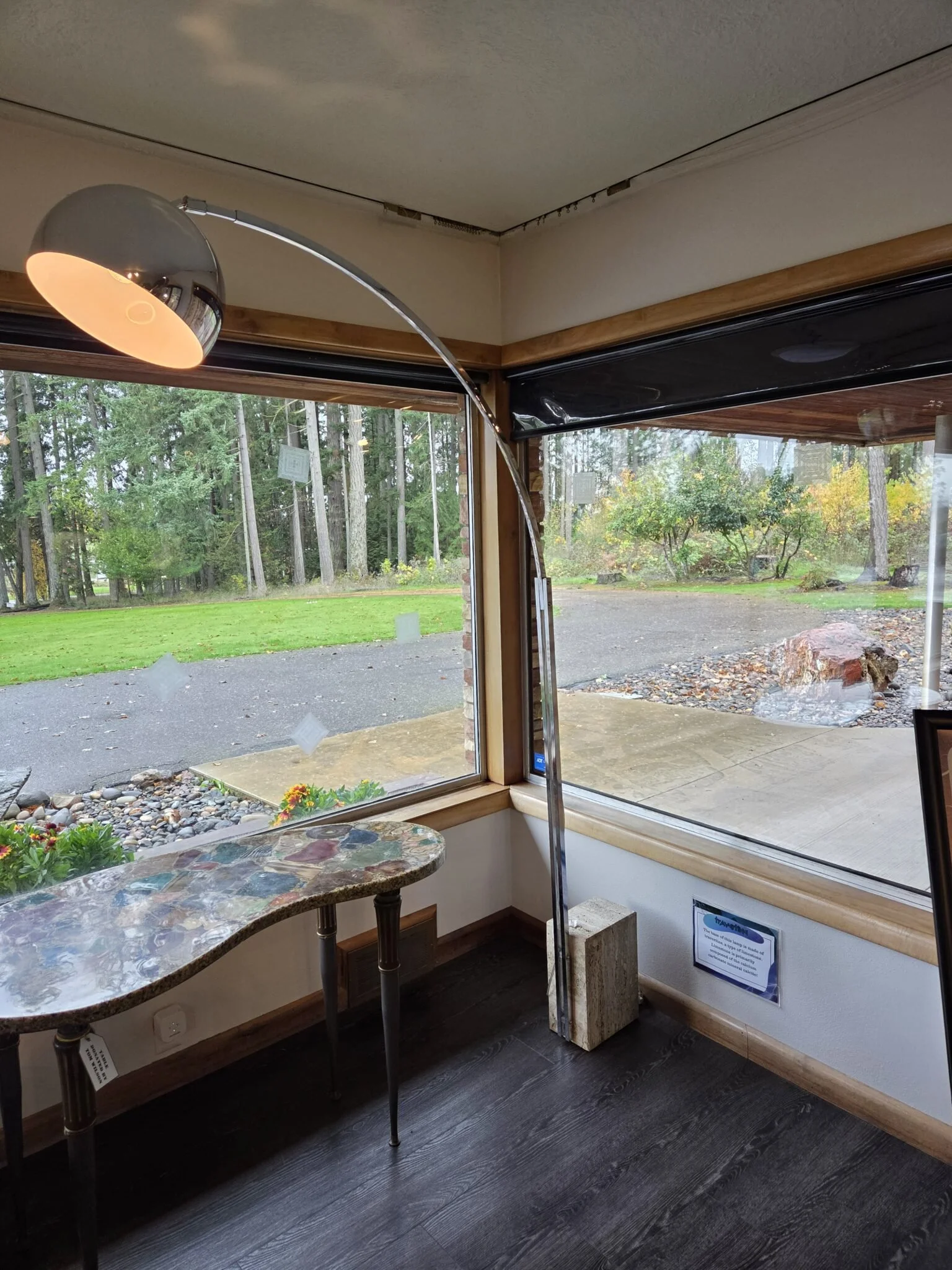Touch-friendly display lamp with a curved metal stem and a rectangular travertine stone base, positioned near a window inside the museum.