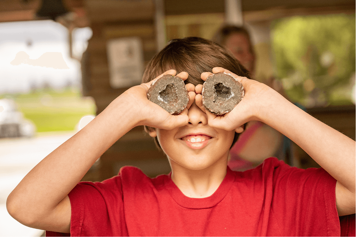 A happy kid holds up two sides of a cracked geode in front of their eyes like rock eyeballs