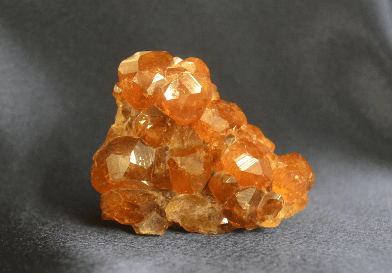 Spessartine garnet crystal cluster showing faceted crystals with vivid orange to amber tones.