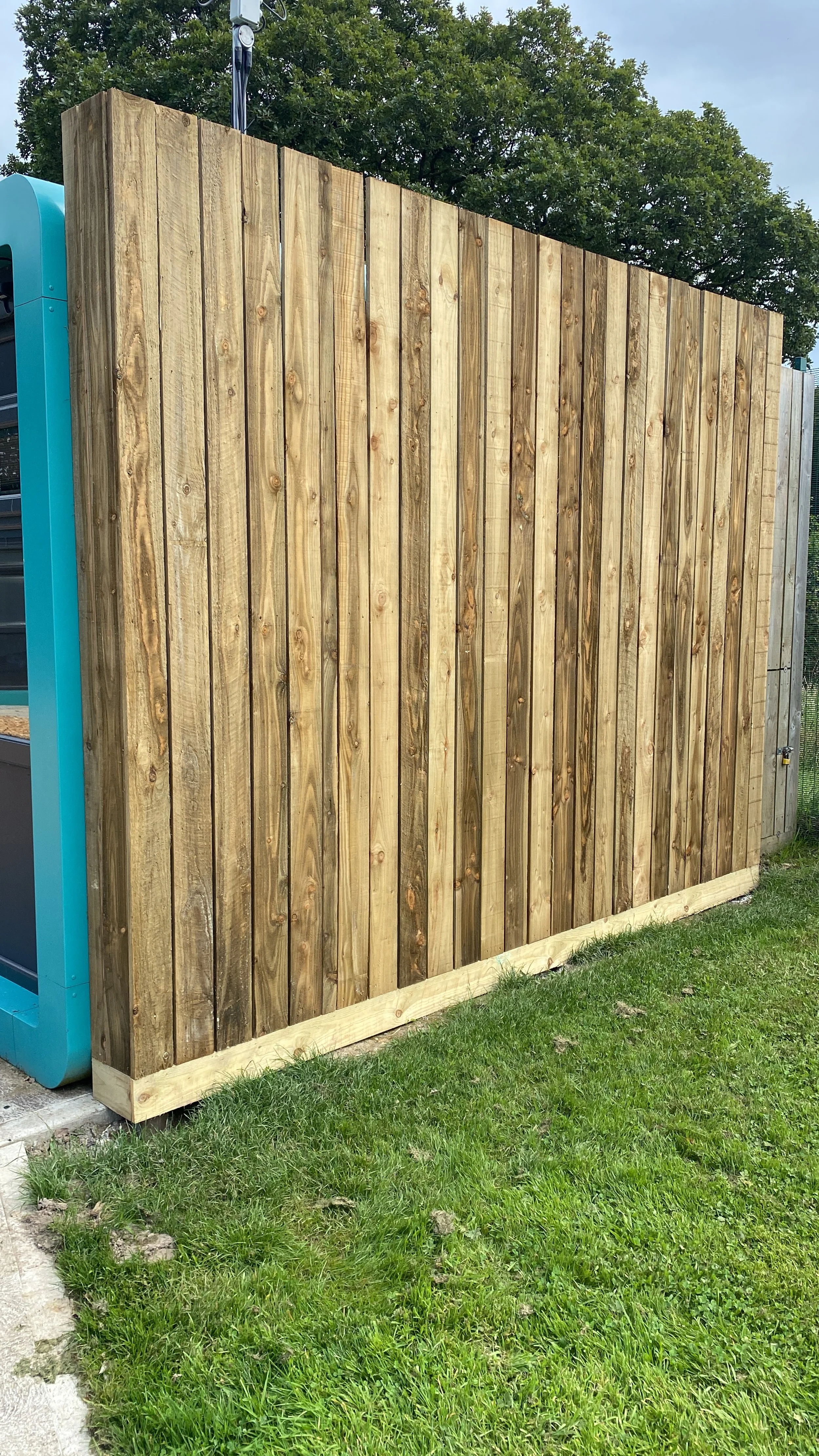 New wooden privacy fence installed, with a grassy yard in front and trees in the background.