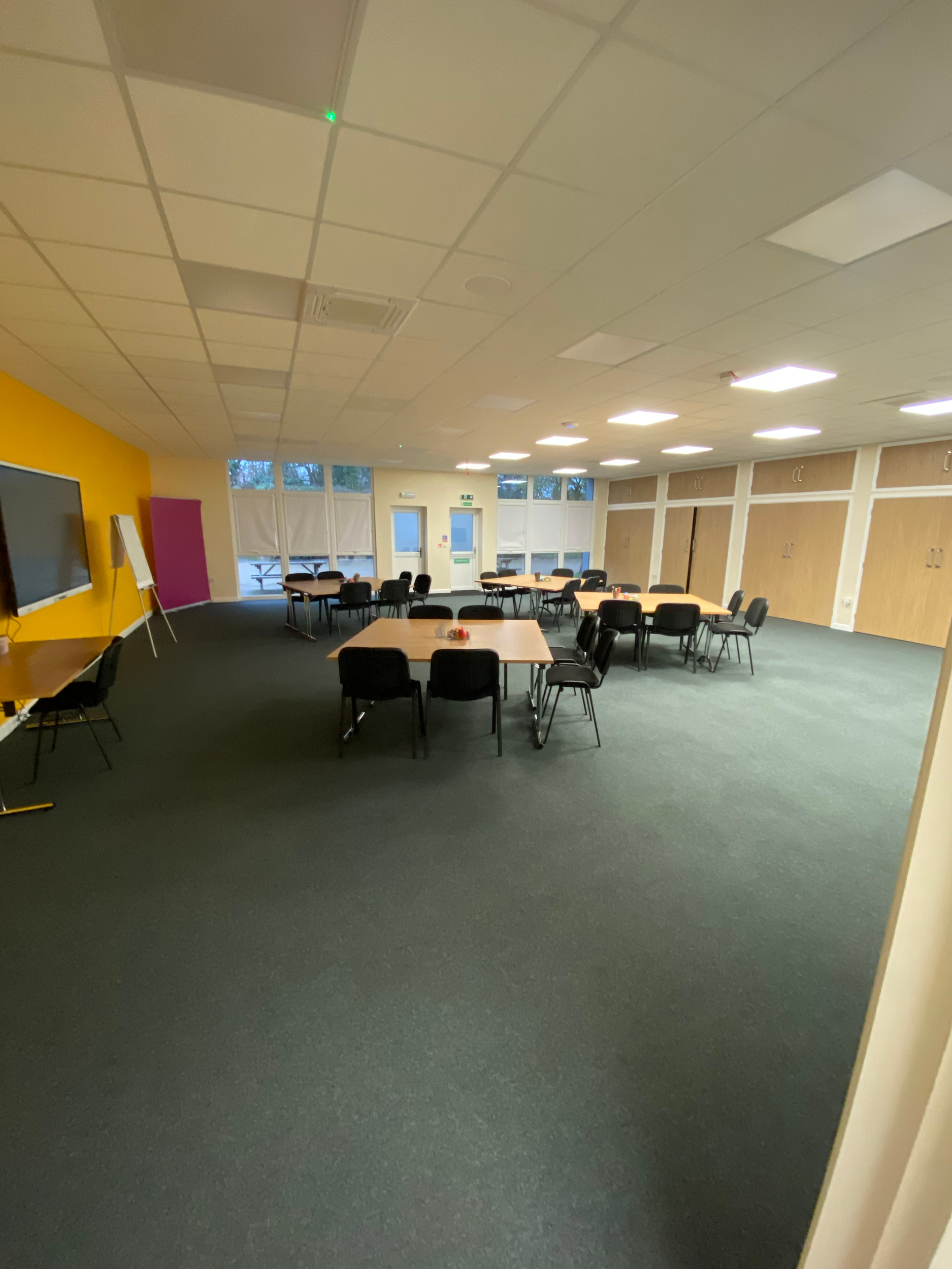 Empty classroom with tables, chairs, and large windows.