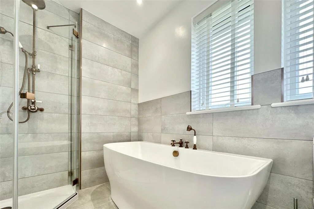 Bathroom with a modern shower, a freestanding bathtub, and a window with white blinds.
