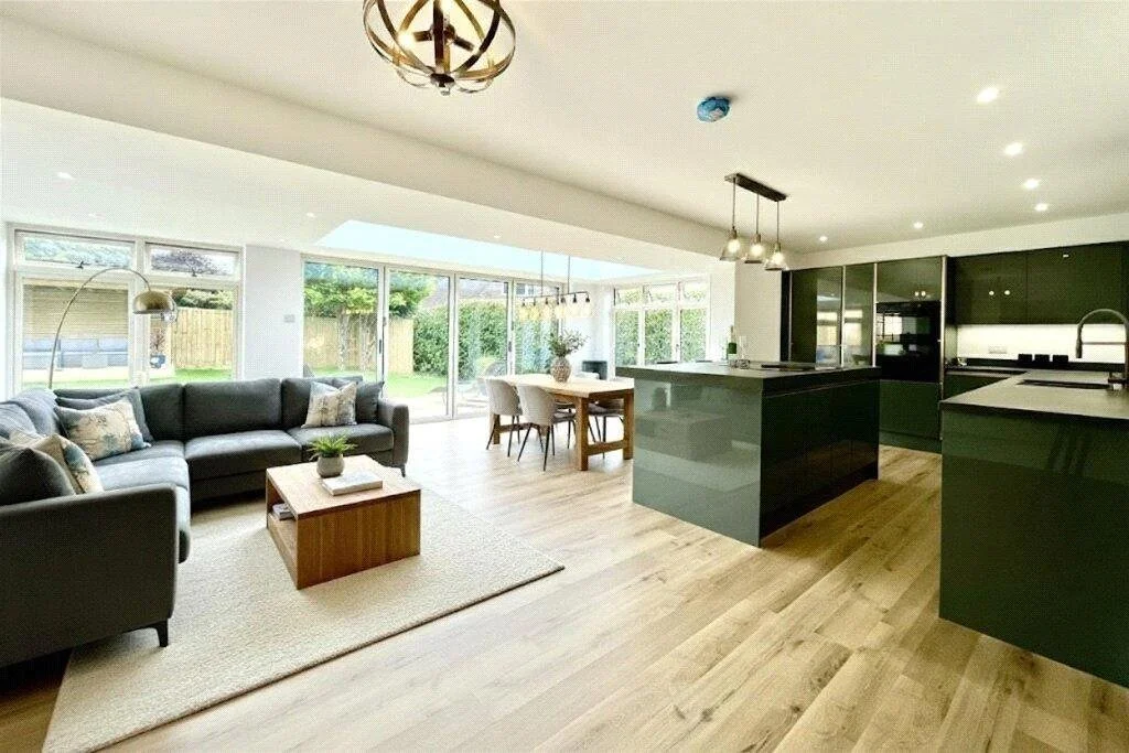 Open-concept living room and kitchen with large windows, a sectional sofa, a coffee table, a dining table, and modern kitchen cabinets with a large island.