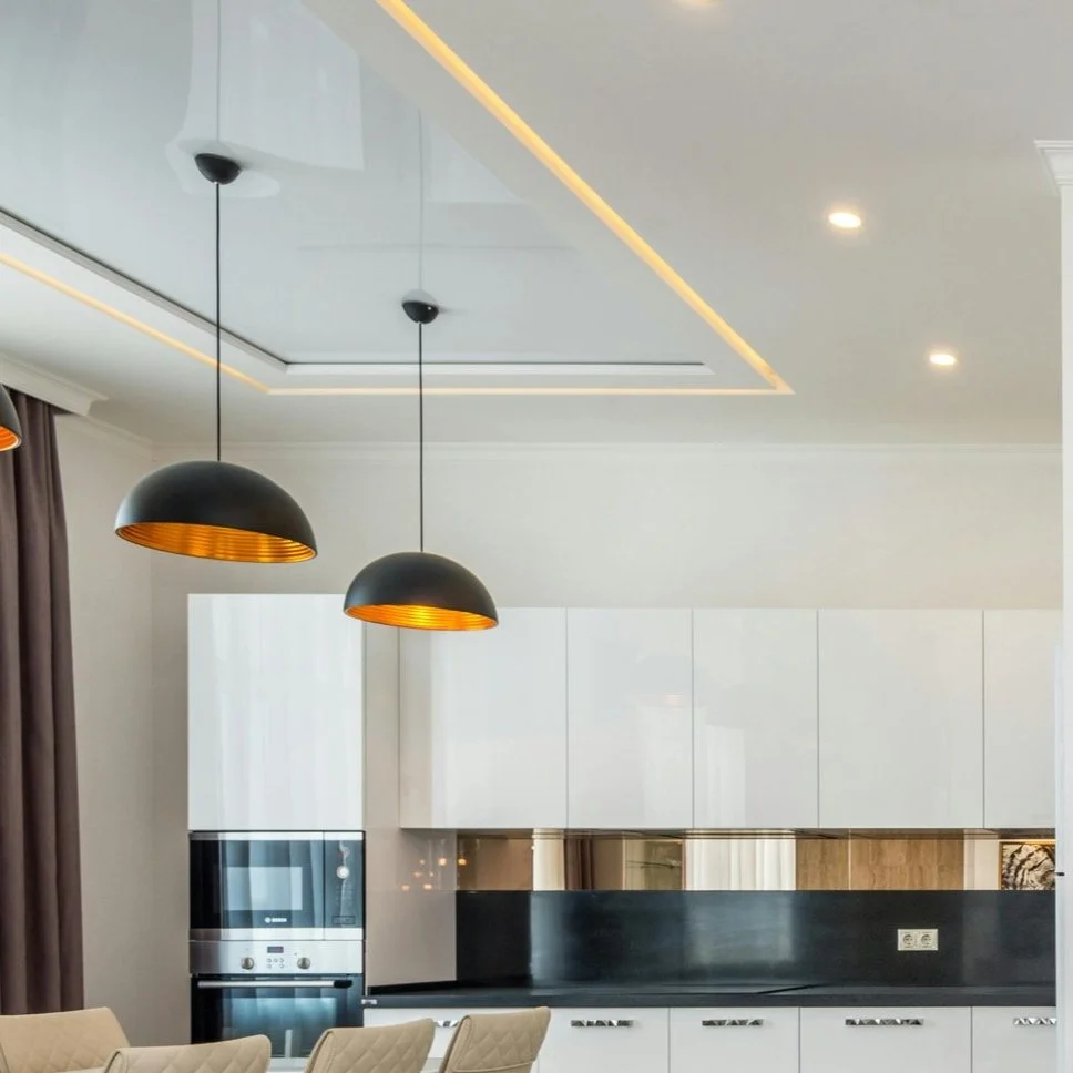 Modern kitchen with white cabinets, black backsplash, built-in oven, and two black hanging pendant lights with gold interiors.